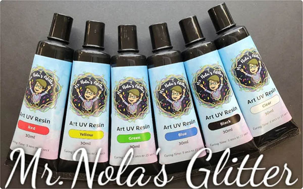 Six Mr. Nola's Glitter Art UV Resin tubes in red, yellow, green, blue, black, and clear.