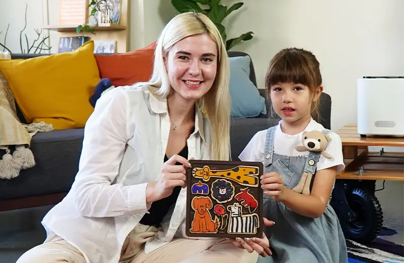A woman and a young girl smiling while holding a wooden animal-shaped puzzle they made together.